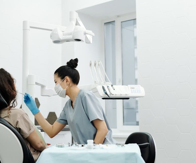 Dentista atendiendo a una paciente en una clínica estomatológica, mientras utiliza instrumentos odontológicos para realizar una revisión bucal.