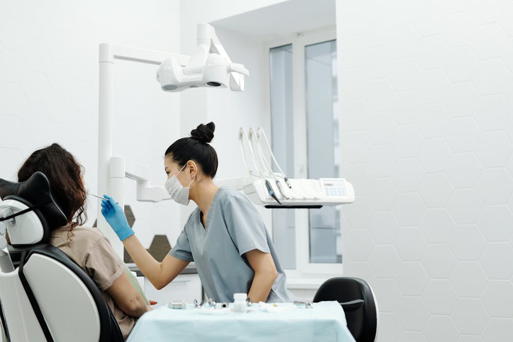 Dentista atendiendo a una paciente en una clínica estomatológica, mientras utiliza instrumentos odontológicos para realizar una revisión bucal.